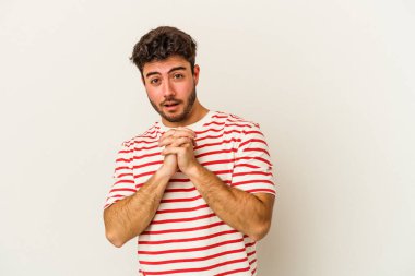 Beyaz arka planda izole edilmiş genç beyaz bir adam şans için dua ediyor, şaşırmış ve ağzını açıp önüne bakıyor..