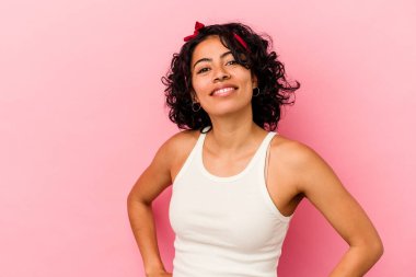 Pembe arka planda izole edilmiş genç kıvırcık Latin kadın ellerini kalçasında tutuyor..