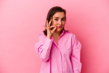 Orta yaşlı, beyaz bir kadın pembe arka planda izole edilmiş, parmakları dudaklarında bir sır saklıyor..