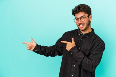 Mavi arka planda izole edilmiş genç beyaz adam işaret parmağıyla fotokopi alanını işaret ederek heyecan ve arzusunu ifade ediyor..