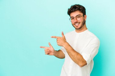 Kafkasyalı genç adam mavi arka planda izole edilmiş. İşaret parmağıyla işaret ettiği için heyecanlı..