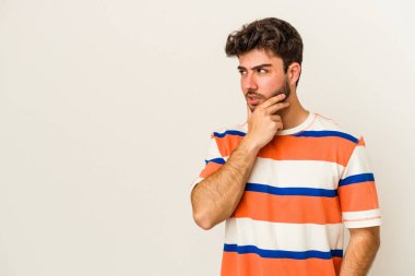 Beyaz arka planda izole edilmiş genç beyaz bir adam kafasının arkasına dokunuyor, düşünüyor ve bir seçim yapıyor..