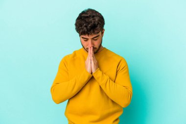 Kafkasyalı genç adam mavi arka planda izole edilmiş dua ediyor, bağlılık gösteriyor, dindar biri ilahi ilham arıyor..