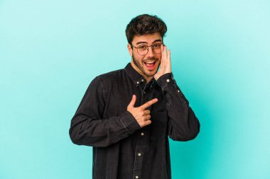 Kafkasyalı genç adam mavi arka planda izole edilmiş. Dedikodu yapıyor, bir şeyleri bildiriyor..
