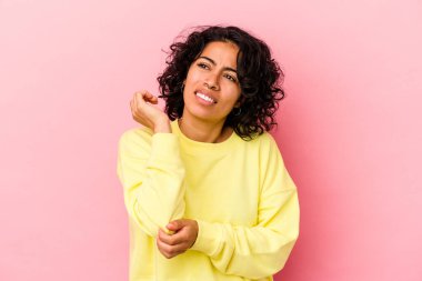 Genç kıvırcık Latin kadın pembe arka planda izole edilmiş, dirsek masajı yapıyor, kötü bir hareketin ardından acı çekiyor..