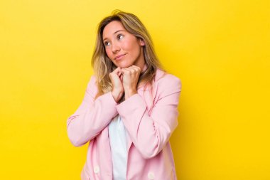 Avustralyalı genç bir kadın yalnız, elleri çenesinin altında, mutlu bir şekilde yan tarafa bakıyor..