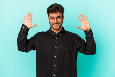 Mavi arka planda izole edilmiş genç beyaz adam hoş bir sürpriz alıyor, heyecanlı ve el kaldırıyor..