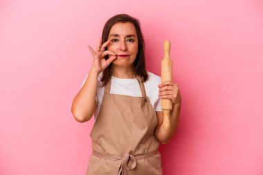 Orta yaşlı pasta şefi kadın pembe arka planda izole edilmiş parmakları dudaklarında bir sır saklıyor..