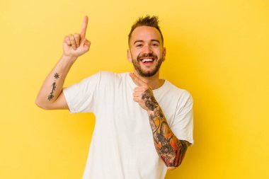 Sarı arka planda izole edilmiş genç dövmeli beyaz adam dans ediyor ve eğleniyor..