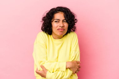 Pembe arka planda soyutlanmış genç kıvırcık Latin kadın omuzlarını silkeliyor ve gözleri açık..