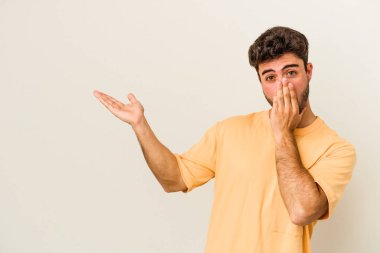 Beyaz arka planda izole edilmiş genç beyaz adam, avuç içi fotokopi alanını elinde tutmaktan etkilenmiş..