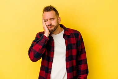 Sarı arka planda izole edilmiş genç dövmeli beyaz adam sıkılmış, yorgun ve dinlenmeye ihtiyacı var..