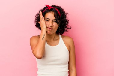 Pembe arka planda soyutlanmış genç kıvırcık Latin kadın yorgun ve uykulu ellerini başının üstünde tutuyor..
