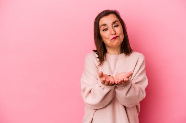 Orta yaşlı beyaz kadın pembe arka planda izole edilmiş dudaklar kıvrılmış ve hava öpücüğü göndermek için avuç içleri tutulmuş..