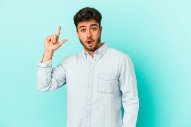 Mavi arka planda izole edilmiş beyaz bir adam ağzı açık bir şekilde üst tarafı işaret ediyor..