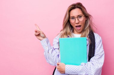 Genç Avustralyalı bir kadın pembe arka planda izole edilmiş. Yan tarafı işaret ediyor.