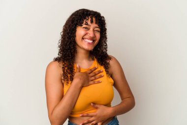 Beyaz arka planda izole edilmiş genç bir ırk kadını mutlu bir şekilde gülüyor ve ellerini karnının üstünde tutarak eğleniyor..