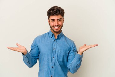 Beyaz arka planda izole genç beyaz adam kollarıyla ölçek yapar, mutlu ve kendinden emin hisseder..