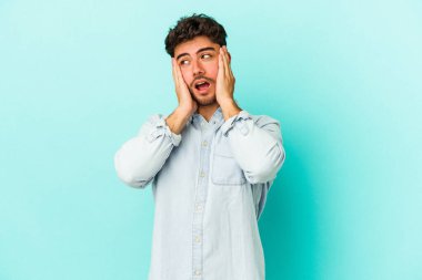 Kafkasyalı genç adam mavi arka planda izole edilmiş korkmuş ve korkmuş..