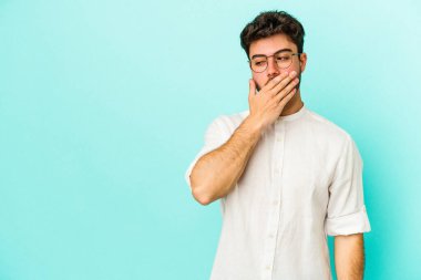 Kafkasyalı genç adam mavi arka planda izole edilmiş. Düşünceli bir şekilde ağzıyla ağzını kapatan bir fotokopi odasına bakıyor..
