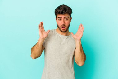 Kafkasyalı genç adam mavi arka planda izole edildi. Şaşırdı ve şok oldu..