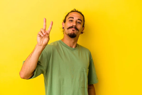 黄色の背景に孤立した長い髪を持つ若い白人男性喜びと屈託のない指で平和のシンボルを示す — ストック写真