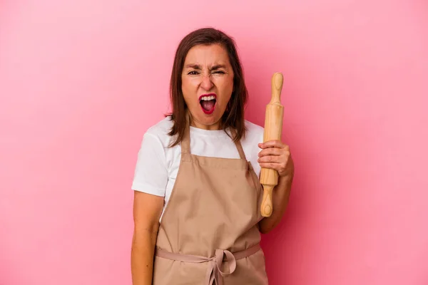 Middle age pastry chef woman isolated on pink background screaming very angry and aggressive.