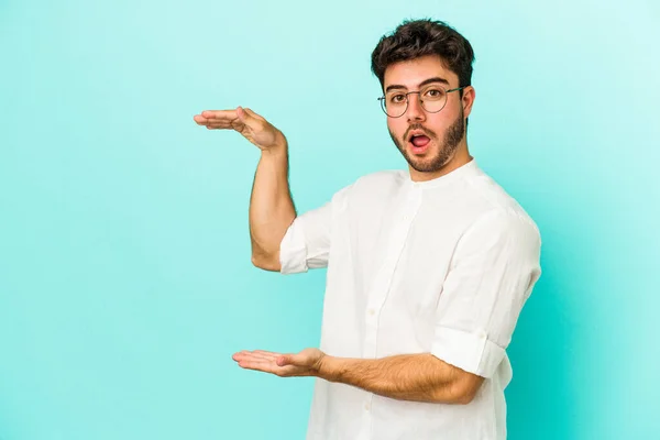 Joven Hombre Caucásico Aislado Sobre Fondo Azul Sorprendido Sorprendido Sosteniendo —  Fotos de Stock