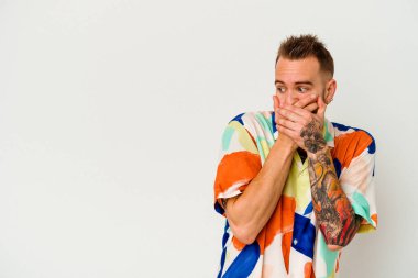 Genç dövmeli beyaz adam beyaz arka planda izole edilmiş. Düşünceli bir şekilde bir fotokopi odasına bakıyor. Ağzını eliyle kapatıyor..