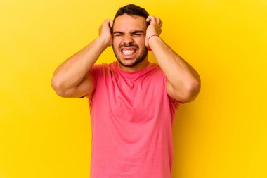 Sarı arka planda izole edilmiş genç beyaz adam elleriyle kulakları örtüyor..