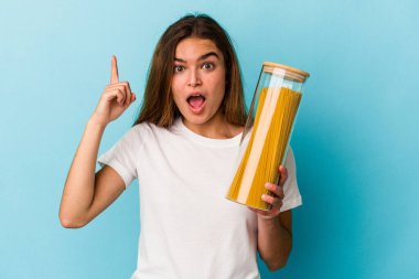 Mavi arka planda izole edilmiş makarna kavanozu tutan beyaz bir kadının bir fikri, ilham verici bir fikri var..