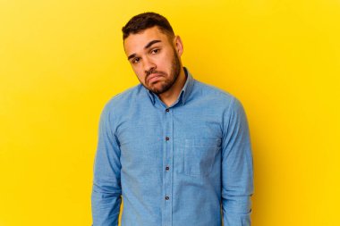 Sarı arka planda izole edilmiş genç beyaz adam omuzlarını silkeliyor ve gözleri açık..