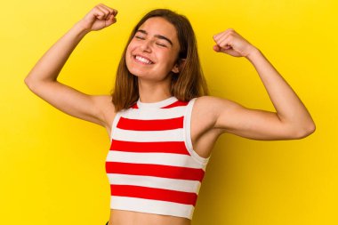 Sarı arka planda izole edilmiş genç beyaz kadın özel bir günü kutluyor, atlıyor ve enerjiyle kollarını kaldırıyor..