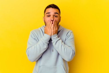 Sarı arka planda izole edilmiş genç beyaz adam elleriyle ağzını kapatırken şok oldu..