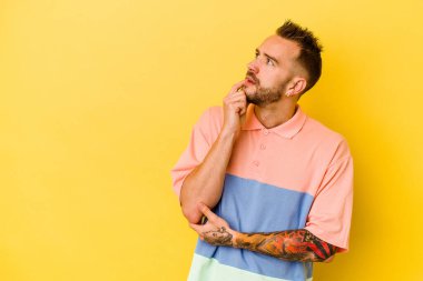 Sarı arka planda izole edilmiş genç dövmeli beyaz adam. Bir şeyin fotokopi odasına baktığını düşünerek rahatlamış..