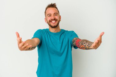 Beyaz arka planda izole edilmiş genç dövmeli beyaz adam hoş bir ifade sergiliyor..
