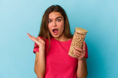 Beyaz arka planda izole edilmiş nohut kavanozu tutan genç beyaz adam şaşırdı ve şok oldu..