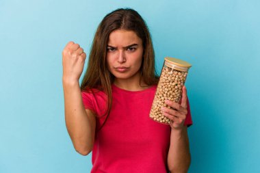 Beyaz arka planda izole edilmiş nohut kavanozu tutan genç beyaz bir adam kameraya yumruk gösteriyor, agresif bir yüz ifadesi..