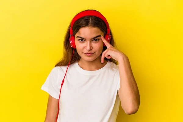Νεαρή Καυκάσια Γυναίκα Ακούγοντας Μουσική Απομονωμένη Κίτρινο Φόντο Δείχνοντας Ναό — Φωτογραφία Αρχείου