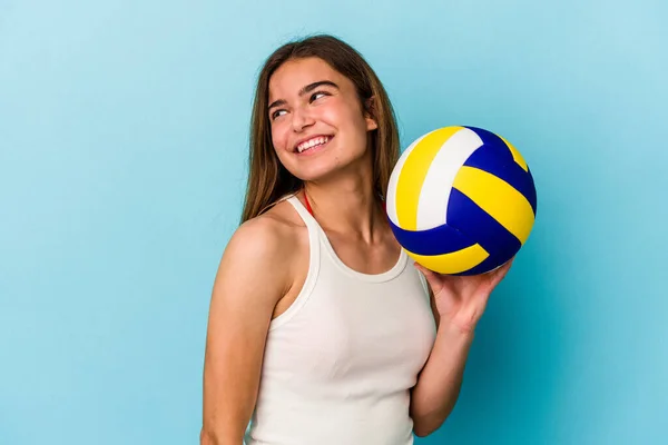 年轻的高加索女子在蓝色背景下打排球 她面带微笑 愉快地看着旁边 — 图库照片