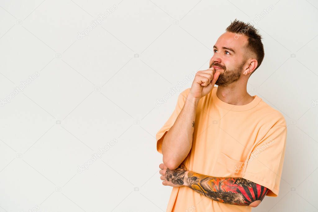 Young tattooed caucasian man isolated on white background relaxed thinking about something looking at a copy space.