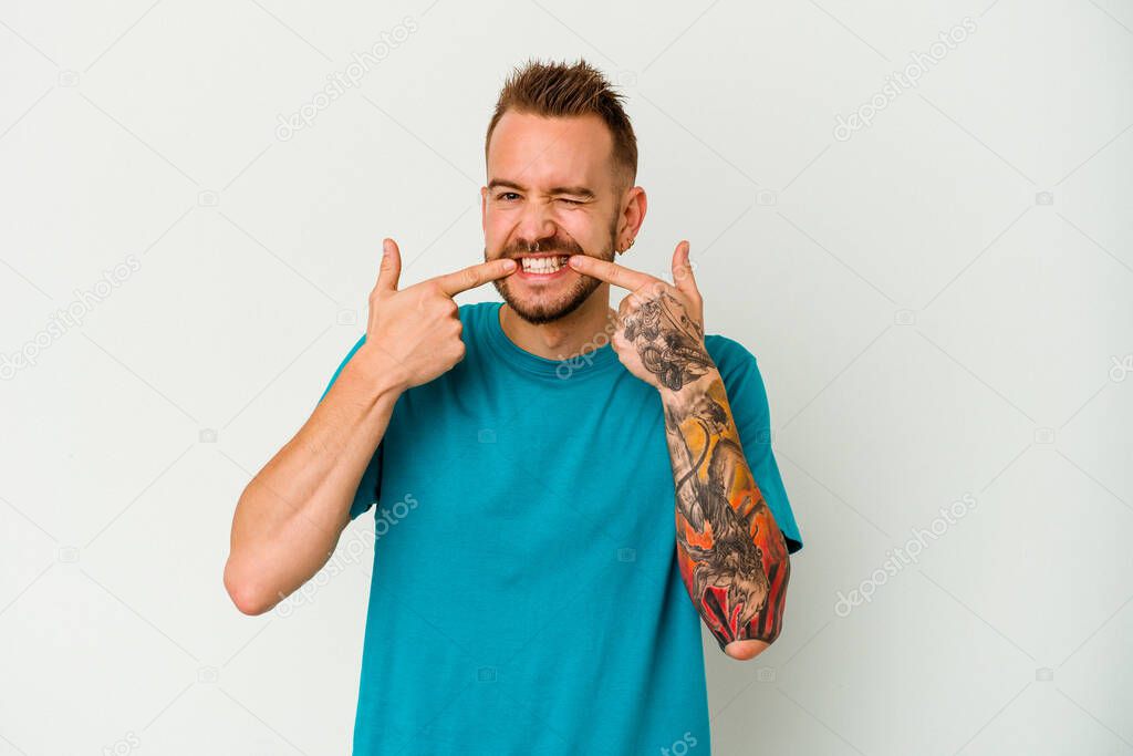 Young tattooed caucasian man isolated on white background smiles, pointing fingers at mouth.