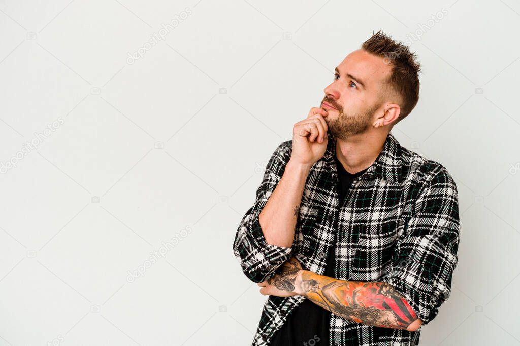 Young tattooed caucasian man isolated on white background relaxed thinking about something looking at a copy space.