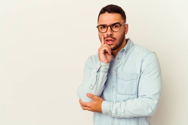 Beyaz arka planda izole edilmiş genç beyaz bir adam şüpheli ve şüpheci bir ifadeyle yana bakıyor..