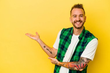 Sarı arka planda izole edilmiş genç dövmeli beyaz adam bir avuç içinde fotokopi alanı ve belinde bir el daha olduğunu gösteriyor..