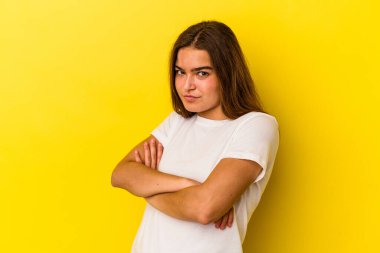 Sarı arka planda izole edilmiş, hoşnutsuzca kaşlarını çatmış, kollarını kavuşturmuş genç beyaz bir kadın..