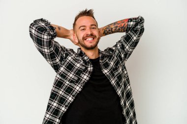 Beyaz arka planda izole edilmiş genç, dövmeli beyaz bir adam. Kendine güveniyor, elleri başının arkasında..