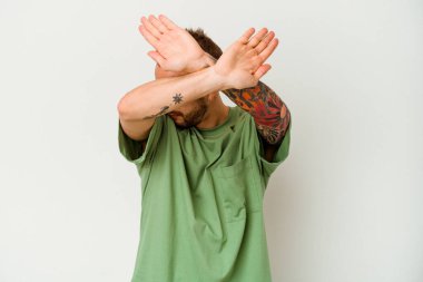 Beyaz arka planda izole edilmiş genç dövmeli beyaz adam iki kolu çapraz tutuyor, inkar kavramı.