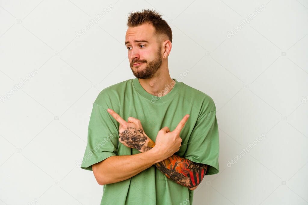 Young tattooed caucasian man isolated on white background points sideways, is trying to choose between two options.