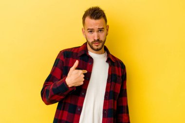 Sarı arka planda izole edilmiş genç dövmeli beyaz adam parmağını gösterip gülümseyerek şaşırdı..